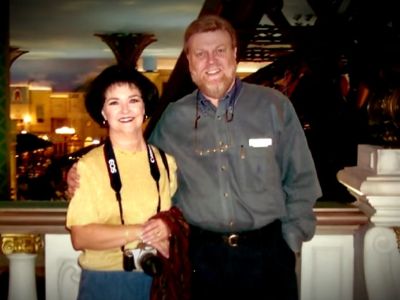 Judy Parsons is holding camera around her neck as Milton Joseph Parsons, Jr. has his arms around her shoulder.